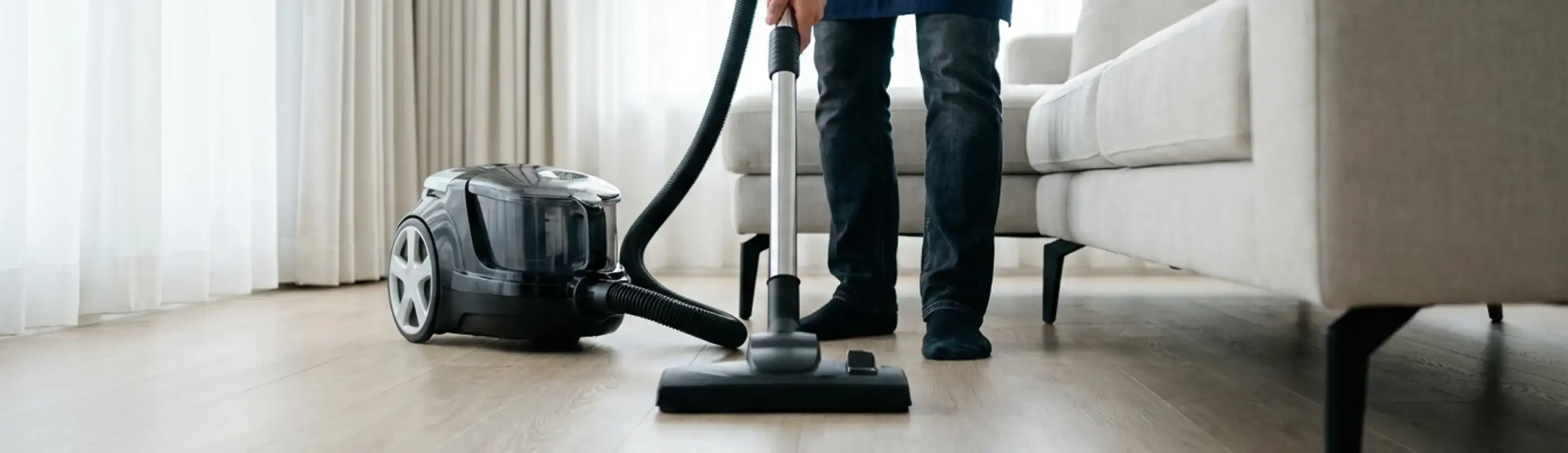 Professional house cleaner vacuuming a living room floor with a canister vacuum cleaner, Pittsburgh, PA.
