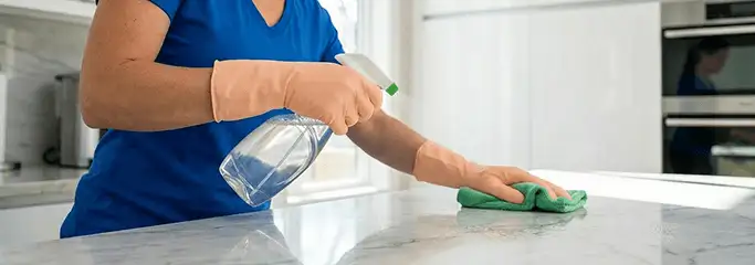 Maid service worker spraying and wiping a kitchen countertop with a microfiber cloth for sanitizing, Pittsburgh, PA.