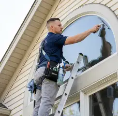Professional window cleaner on a ladder using a squeegee to clean an exterior arched window, Pittsburgh, PA.