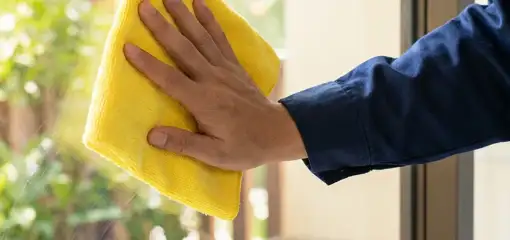 House cleaner wiping a glass window with a yellow microfiber cloth for streak-free cleaning, Pittsburgh, PA.